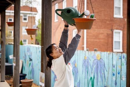 A student stretches her arms to water a plant pot at a volunteer site.